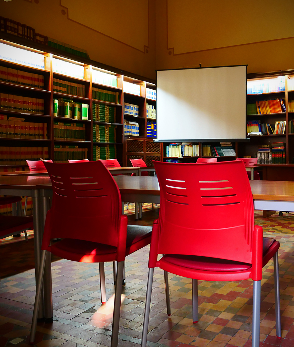 Pequeña sala de presentaciones situada en uno de los espacios de la Facultad de Derecho. El lugar cuenta con estanterías, un proyector y diversas sillas y mesas